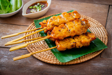 Grilled chicken skewers on banana leaf served with spicy dipping sauce and vegetable