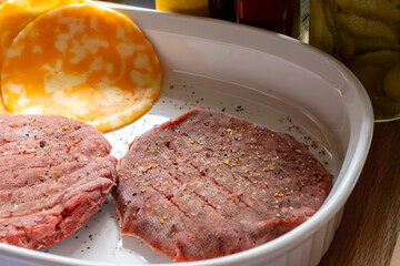 Two frozen beef burgers with seasonings and cojack cheese slices.  Grill is preheating.