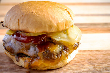 Straight from the grill, burger patty topped with cojack cheese, grilled onions, dill pickles, ketchup and mustard on a toasted bun.   On a wooden board.