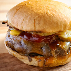Straight from the grill, burger patty topped with cojack cheese, grilled onions, dill pickles, ketchup and mustard on a toasted bun.   On a wooden board.