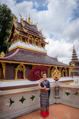 Woman wearing Thai dress visits beautiful temple in Thailand.