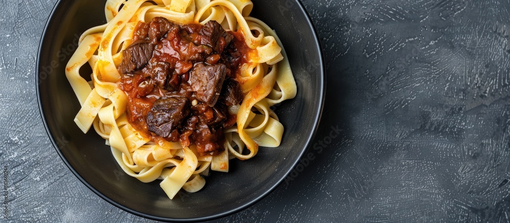 Poster Top view of a black bowl filled with fettuccine pasta and beef ragout sauce on a grey backdrop, ideal for adding text or images (copy space image).