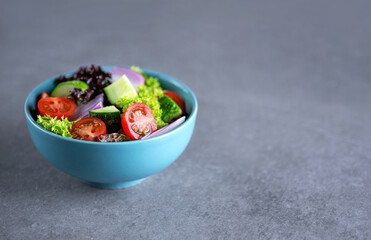 Healthy salad of fresh vegetables in a plate on a gray background.