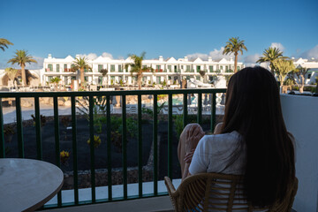 A woman is sitting on a chair on a balcony overlooking a pool