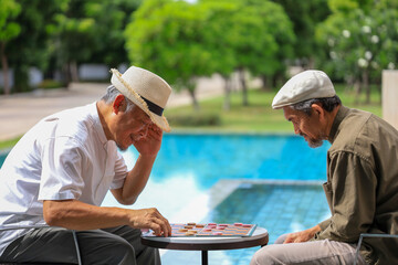 Two senior asian friend are enjoy playing checkers board game at the tropical resort for retirement...