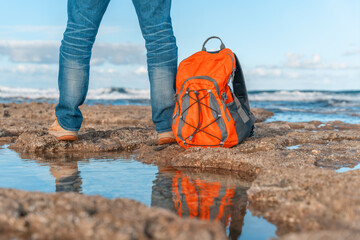 Man Standing On Rocky Beach With Orange Backpack