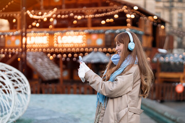 Woman Using Smartphone at Festive Winter Market With String Lights