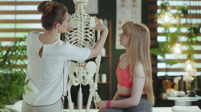Healthcare time. concerned massage therapist woman in massage cabinet with teenage client and skeleton.