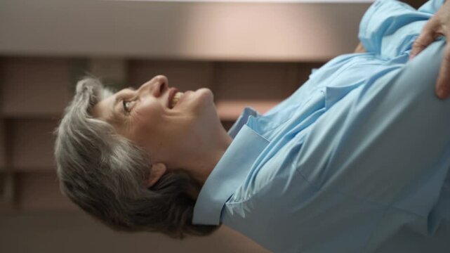 A senior woman is performing a backbend stretch exercise while lying on a bed. She is wearing a blue shirt and has gray hair. This video shows how seniors can stay active and healthy through simple
