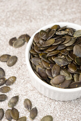 Peeled pumpkin seeds in plate on gray stone background, close-up