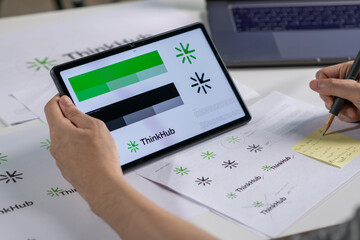 Male Asian graphic designer working in an office studio, using tablet, designing logos and showcasing the corporate identity and logo design process.