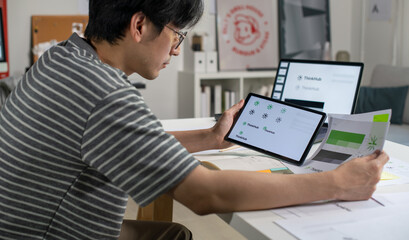 Male Asian graphic designer working in an office studio, using tablet, designing logos and showcasing the corporate identity and logo design process.