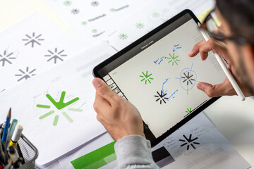Close-up shot of a graphic designer making notes on logo designs, using a tablet, designing logos, and showcasing the corporate identity and logo design process.
