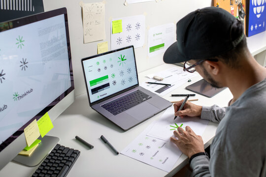 Asian graphic designer making notes on logo designs, using computers, designing logos, and showcasing the corporate identity and logo design process.
