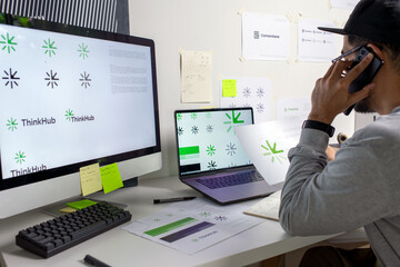 Asian graphic designer making calls discussing about logo designs, using tablet and laptop,...
