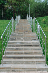 stone staircase with metal railings in city park in summer day, green grass on sides, place for walking and cardio training, no people, vertical photo