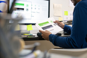 Candid shot of Asian graphic designer inspecting logo designs, using computers, designing logos, and showcasing the corporate identity and logo design process.