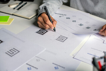 Close-up shot of a graphic designer making notes on logo designs and showcasing the corporate...