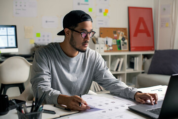 Candid shot of Asian graphic designer inspecting logo designs, using computers, designing logos,...