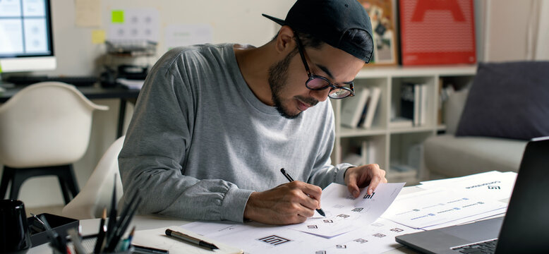 Asian graphic designer making notes on logo designs, using computers, designing logos, and showcasing the corporate identity and logo design process.