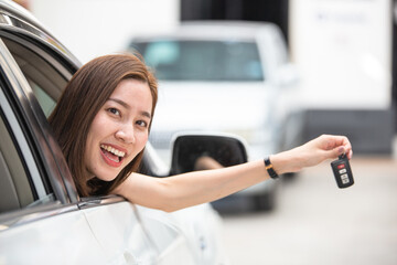 Smiling Asian woman sitting in the car and showing remote key. Customer purchasing new car, auto rental service, Tourist ready for vacation. Satisfied service business