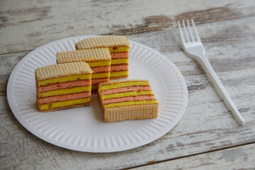 Sliced pieces of layered sponge cake on a white disposable plate with a disposable fork on a wooden table