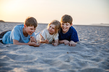Three children playing with sand on sunset ocean beach. happy family, two school boys and one little preschool girl. Siblings having fun together. Bonding and family vacation in Andalucia, Spain