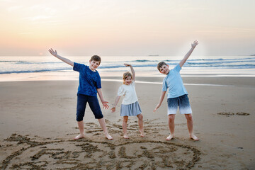 Three children, happy siblings on ocean beach at sunset. happy family, two school boys and one little preschool girl. Brothers and sister having fun, Spain, Costa del Sol