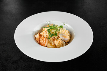 Seafood Risotto with Scallops and Shrimp in a White Plate on Black Background