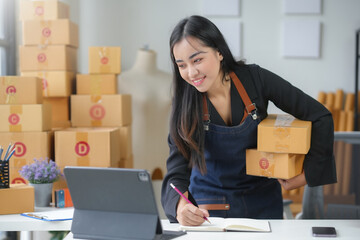 Asian sme business owner holding parcel looking at tablet and taking notes