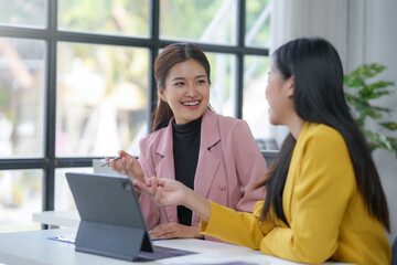 Two young businesswomen collaborating and discussing a project on a tablet in a modern office