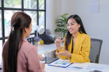 Obraz premium Smiling asian businesswoman explaining project to a colleague