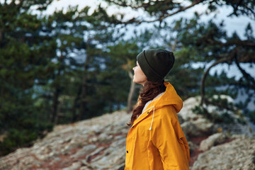 A solitary figure in a vibrant yellow raincoat stands atop a majestic mountain, gazing towards the distant horizon