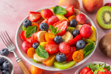 Summer fruit salad in a bowl on pink background with fork. Healthy vegan food for breakfast. Mixed tropical fruits berries for vegetarian diet lunch. Close up