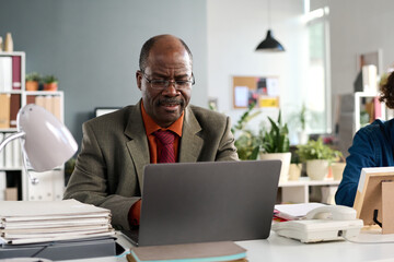 Portrait of African American senior man using laptop working in open office in contemporary inclusive business setup
