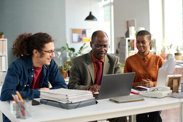Portrait of senior African American man using laptop in inclusive office setup with two young...