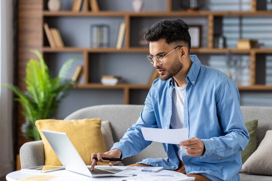 Young man working from home with laptop and documents in modern living room