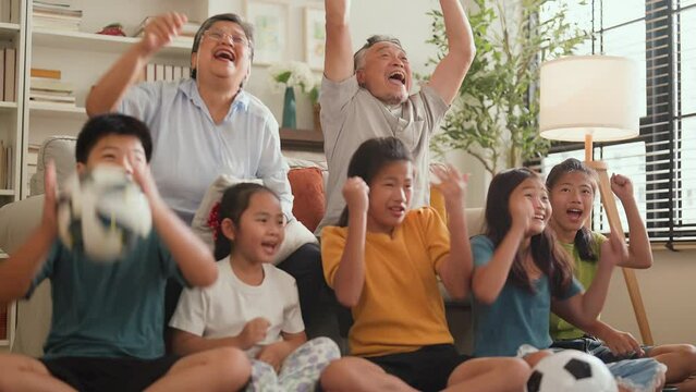 Cheerful multi-generation asian family having fun while watching a game of their favorite sports team on TV at home happy exciting Family cheering football soccer in living room at home 