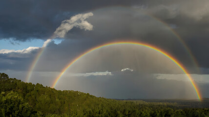 A rainbow arches over a field and river in a vibrant landscape
