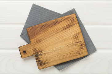 Cutting board with napkin on wooden background, top view