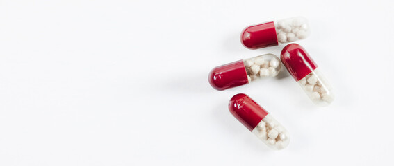 Red and white pills are scattered on a white surface, with the white background taking up most of the image. Red and white pills on white background.