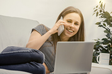 Young woman working from home on laptop and talking on phone