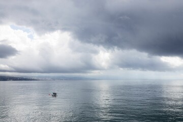 Small boat floating on a calm sea under a dramatic cloudy sky with a distant city skyline