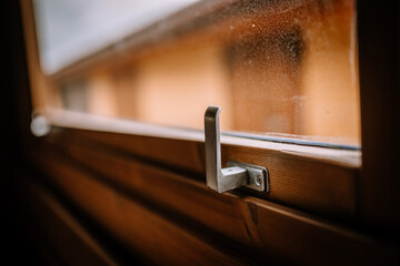 Close-up of a metal latch on a wooden window frame, with a blurred view of the outside. Copy space.