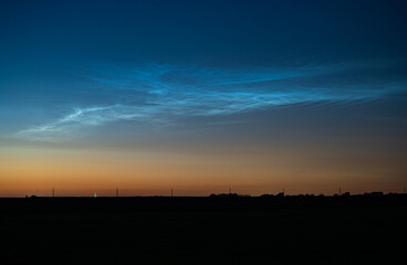 Bright silvery blue noctilucent clouds (NLC) stand out against the evening twilight sky on a...