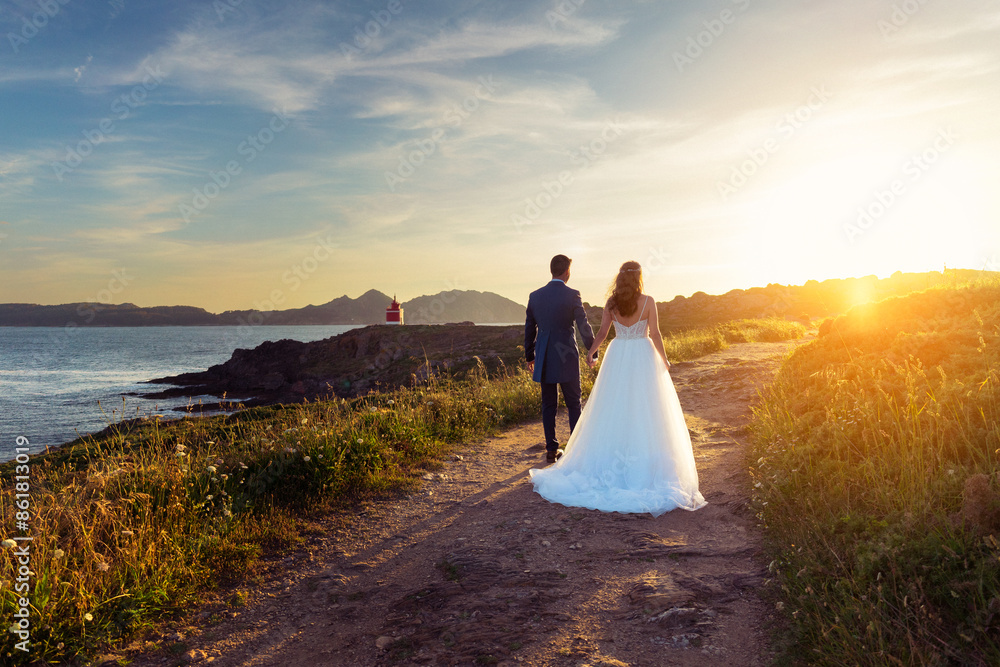 Wall mural Bride and groom walking towards a lighthouse at sunset