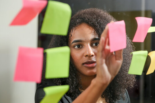Mixed race young woman at the office looking for post notes at the window.