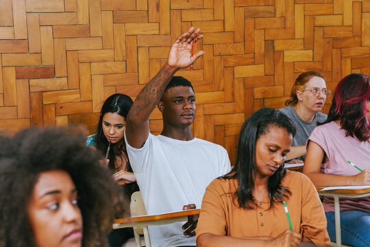 Young black college student in the classroom with his hand raised to ask a question.