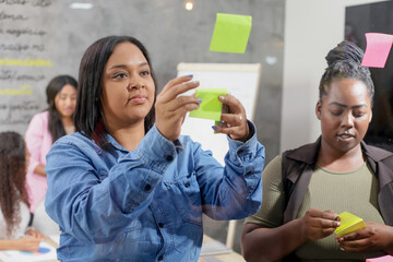 Creative team pasting colorful sticky notes on the window during brainstorming in the office.