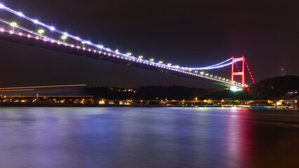 Fototapeta premium The illuminated bridge on the Bosphorus strait late at night in Istanbul with light trails from the ships